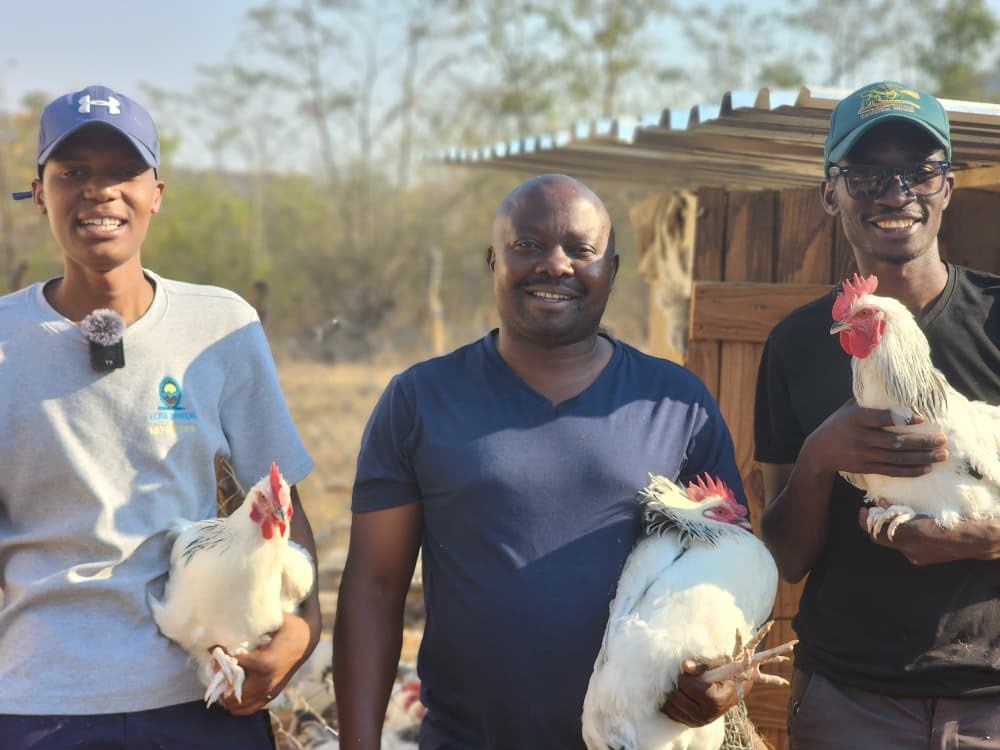 Three smiling men standing outdoors, each holding a white chicken