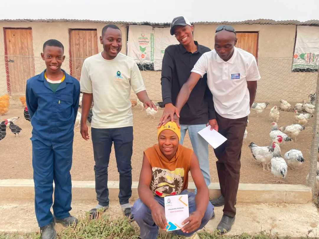The Elite Breeds & Hatcheries team smiling outside a poultry house, with chickens behind a wire fence
