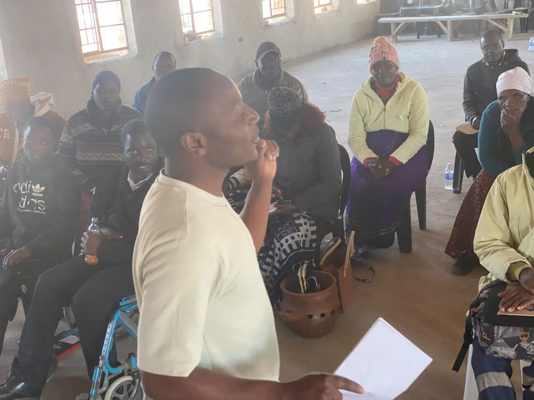 A team member speaking to a seated group of farmers during a training session